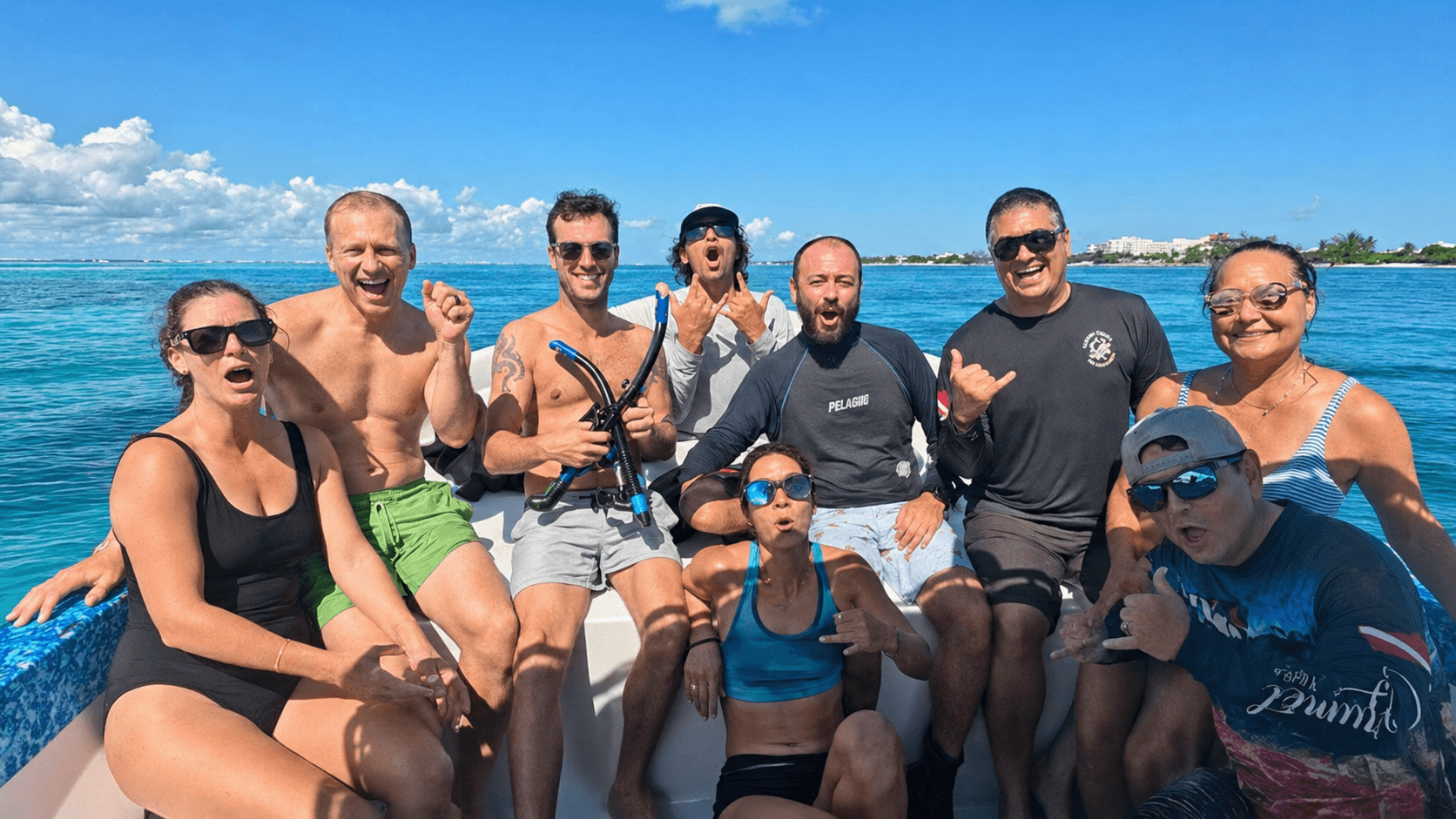 Group of smiling people in swimwear posing on a boat in the bright blue ocean.