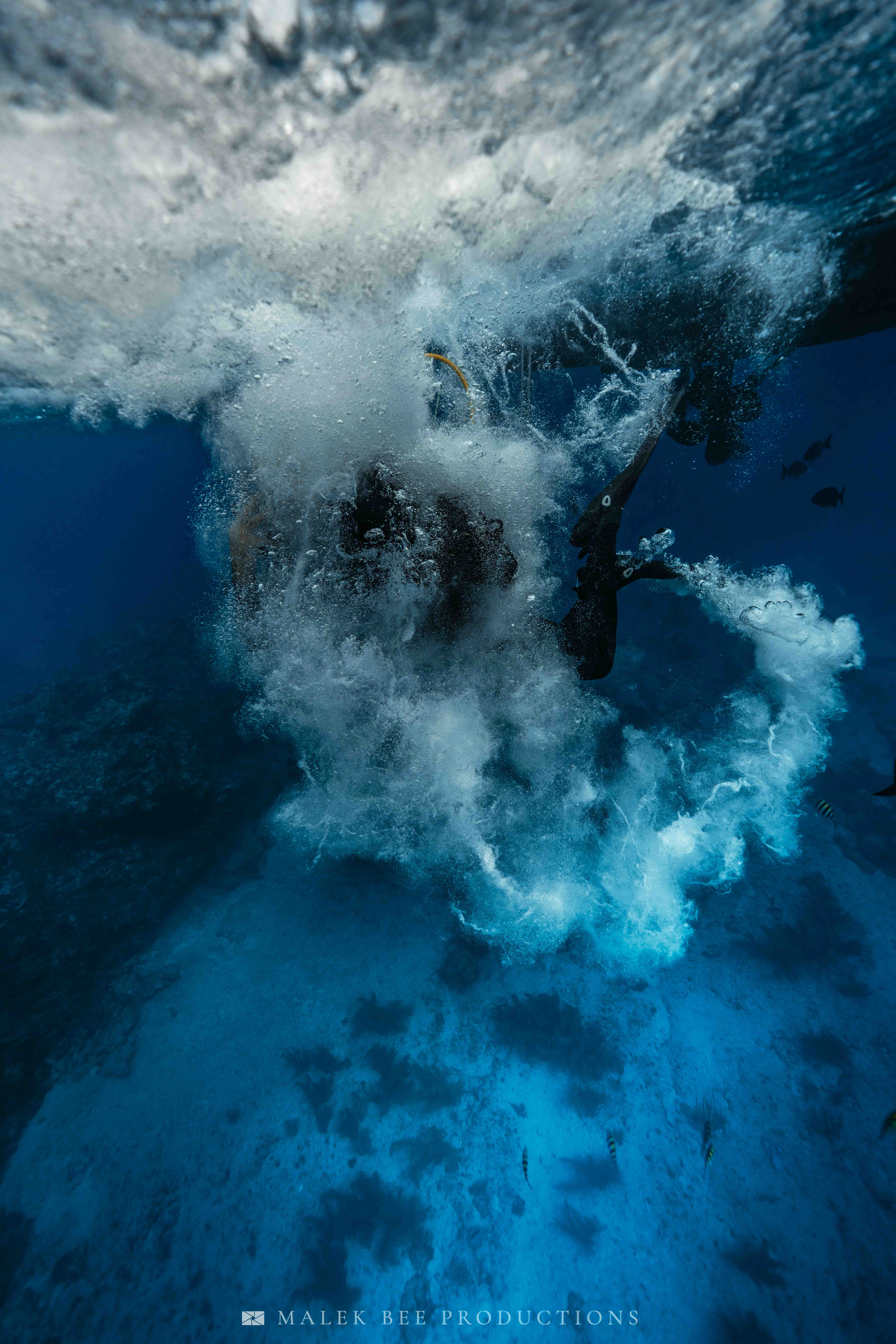 Scuba diver entering deep blue water, creating a massive explosion of white bubbles.